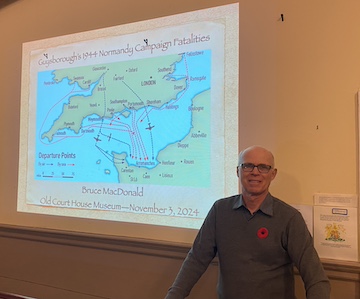 Bruce MacDonald standing in front of Title Slide from Normandy presentation